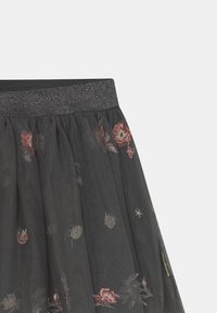 Falda de tul negra con un diseño fruncido, que presenta patrones florales bordados en rojo y crema, y una cinturilla elástica negra brillante.