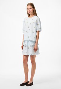 Svetle modrý texturovaný top s krátkým rukávem a odpovídající sukně, zdobené květinovými vzory v žluté a fialové barvě, s vrstvenými designovými detaily.