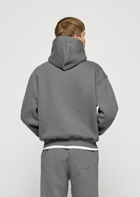 Gray hoodie with a large hood, made from soft fabric. Features drop shoulders and ribbed hem. Worn over matching gray pants.