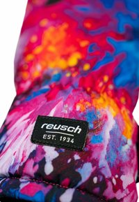 Bunte gemusterte Handschuhe in einer Mischung aus Pink, Blau und Gelb, mit einem schwarzen Etikett, auf dem "reusch EST. 1934" steht.