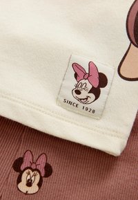 Puuvillane riietus, millel on kreemikas ülemine osa koos Minnie Mouse'i sildiga ja pruun ribakujuline allosa, millel on väike Minnie Mouse'i muster.