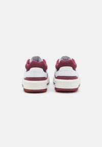 Białe i burgundowe sneakersy wykonane z siateczki oraz materiałów syntetycznych, z wyściełanym kołnierzem, gumową podeszwą oraz logo Lacoste na pięcie.