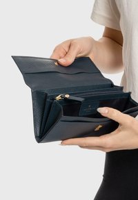 Billetera de cuero azul marino con un acabado texturizado, que cuenta con varios compartimentos, un bolsillo con cremallera y herrajes en tono dorado. La apertura es amplia.