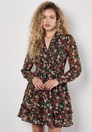 Long-sleeve, floral dress in dark green. Features a smocked waist, ruffled hem, and a V-neckline with a vibrant mix of orange and white flowers.