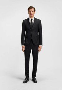Costume noir avec un design à un bouton, revers en notch et deux poches avant. Associé à une chemise blanche, une cravate noire et des chaussures noires brillantes.