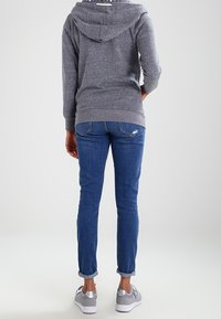 Felpa grigia con cappuccio e cordino, abbinata a jeans blu con risvolto e sneakers grigie. Texture liscia; design informale.