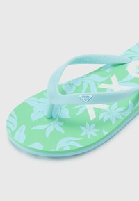 Infradito verdi con superficie texturizzata e motivi floreali azzurri. Cinghie in gomma blu e un piccolo logo dettagliato sulla soletta.