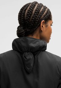 Sorte, letvægtsjakke med høj krave og rynket detalje bagpå. Glat tekstur og minimalistisk design, der er egnet til forskellige anledninger.