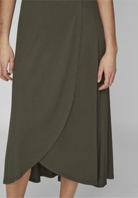 Olijfgroene wikkelrok tot op de knie, gemaakt van zachte stof, met een gebogen zoom en zichtbare stiksel details.