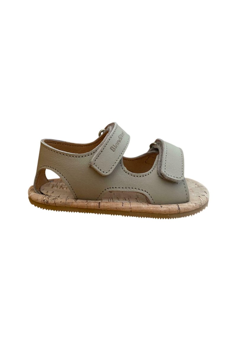 Sandaña infantil de cuero color gris claro con dos correas ajustables, suela de corcho, detalles recortados y suela de goma texturizada.