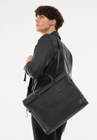 Borsa a tracolla in pelle nera con manici doppi, texture liscia e dettagli di cucitura discreti. Tracolla regolabile per una maggiore versatilità.