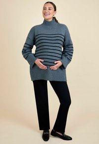Szürke csíkos garbó pulóver bordázott textúrával, laza ujjakkal és kényelmes szabással, fekete slim fit nadrággal és fekete loafer cipővel párosítva.