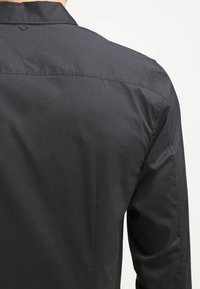 Camisa negra de botones con una textura de tela suave, cuello clásico y un sutil diseño de yugo en la parte posterior.