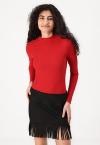 Rode geribbelde lange mouwen top met een golvende halslijn, gecombineerd met een zwarte suède mini rok met franjen langs de zoom.