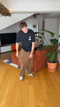 Calças cargo castanhas com vários bolsos, ajuste descontraído e textura lisa, combinadas com uma t-shirt preta com um design gráfico.