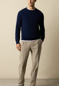 Granatowy sweter dzianinowy z okrągłym dekoltem, ściągaczami przy mankietach i u dołu. Połączony z jasnobeżowymi spodniami z korduroju w pionowe paski.