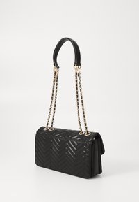 Schwarze gesteppte Handtasche mit Fischgrätenmuster, gekennzeichnet durch eine strukturierte Form, zwei Kettenriemen in Goldtönen und einen flachen, glatten Boden.