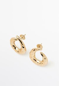 Náušnice ze zlaceného kovu s krouceným, organickým tvarem. Mají lesklý povrch a bezpečné zapínání na šroubek.