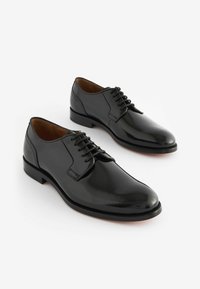 Chaussures habillées en cuir noir avec une finition brillante, bout rond, laçage à l'avant et talon plat, présentant un design lisse et élégant.