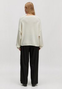 Oversized crèmekleurige trui met verlaagde schouders en geribbelde onderkant, gecombineerd met losse zwarte broeken. Glad textuur, minimalistisch ontwerp.