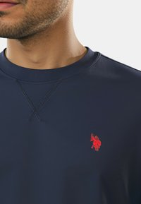 Felpa blu navy realizzata in tessuto liscio, con scollo rotondo, dettaglio a punto croce e un piccolo logo rosso ricamato sul petto.