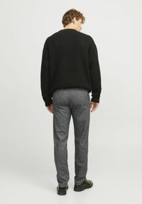 Zwarte textuurtrui, relaxte pasvorm, gecombineerd met grijze gemusterde broek en zwarte schoenen. Gezien vanuit de achterkant. Minimalistisch ontwerp en neutrale kleuren.