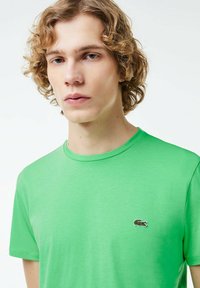 Zielony bawełniany t-shirt z okrągłym dekoltem i krótkimi rękawami, z małym haftowanym logo krokodyla po lewej stronie klatki piersiowej.