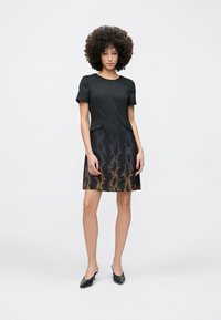 Robe noire avec manches courtes, encolure ronde et un motif dégradé passant du noir à l'orange. Comprend des poches latérales.