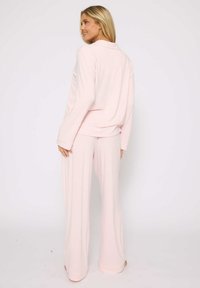 Light pink loungewear set featuring a long-sleeve button-up top and wide-leg pants, made from soft, smooth fabric. Minimal detailing.
