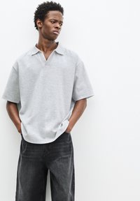 Grå, kortærmet polo skjorte med V-hals design. Materialet ser blødt ud og har en afslappet pasform. Sammen med mørke, løse jeans.