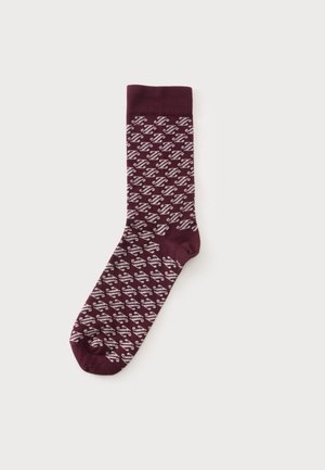 Une chaussette bordeaux unique avec un motif zigzag diagonal blanc et un bord-côtes sur un fond clair uni.
