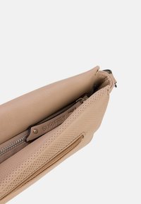 Pochette in pelle beige con accenti perforati e scomparto con zip. Presenta una finitura liscia e un discreto etichetta con il logo.