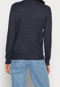 Mörk marinblå stickad tröja med långa ärmar, ribbade mudd och nederkant. Bärs med ljusblå denimjeans som visar en avslappnad passform.