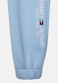 Lyseblå bomulds-joggingbukser med ribbet cuff, prydet med broderet "TOMMY HILFIGER" og logo detaljer i hvid og rød, struktureret overflade.