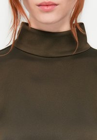 Mørkegrønn høyhalset genser laget av glatt stoff, med en tettsittende silhuett og subtil glans. Minimalistisk design uten synlige mønstre eller accenter.