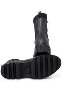 Botas de tobillo de goma negras con una superficie texturizada y cremallera lateral, con suela acanalada y lengüeta trasera para ponerlas y quitarlas fácilmente.