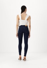 Vit texturerad crop top med breda axelband, kombinerad med mörkblå smala jeans med hög midja och bakfickor. Bruna klacksandaler.
