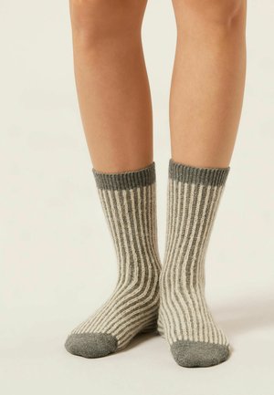 Chaussettes rayées en beige clair et gris avec une texture côtelée. Présentent des poignets et des embouts contrastants gris. Le tissu est doux et tricoté.