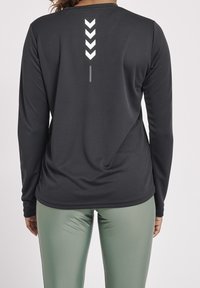 Langärmliges schwarzes Sportshirt mit strukturierter Oberfläche, das ein vertikales weißes Chevron-Muster auf der Rückseite aufweist.