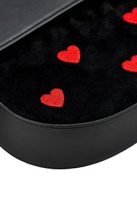 Černá kulatá nádoba s měkkým černým vnitřním obložením, zdobená vyšívanými červenými srdíčky, lemovaná hladkým černým materiálem.