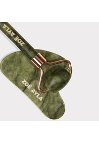 Rouleau facial en jade vert avec des accents métalliques en or rose reposant sur une pierre de gua sha en jade assortie, tous deux marqués "Zoë Ayla" sur fond blanc.