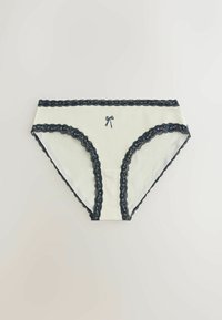 Białe majtki damskie z czarną koronkową lamówką przy pasie i nogawkach, ozdobione małą czarną kokardką z przodu na środku.