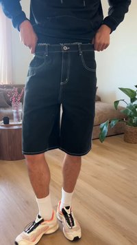Άτομο που φοράει μαύρο σορτς, λευκές κάλτσες και αθλητικά παπούτσια, προσαρμόζοντας τη μέση μέσα σε ένα σαλόνι με φυτά και έπιπλα.