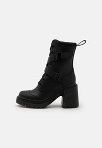 Bottines noires à talon épais, en matériau synthétique lisse, avec un laçage à l'avant et des sangles réglables au niveau du milieu du pied.