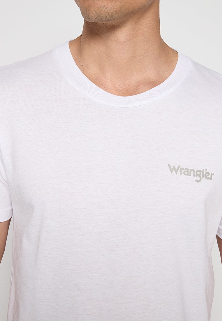 Biała bawełniana koszulka z okrągłym dekoltem i krótkimi rękawami, z małym szarym logo "Wrangler" na piersi. Gładka tekstura.