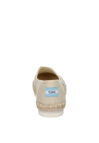 Scarpa slip-on in tela beige con suola in iuta intrecciata, caratterizzata da un'etichetta con il logo TOMS azzurro sul tallone. Design semplice e leggero.