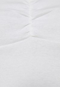 Tissu blanc à côtes avec une texture froncée au centre, présentant des lignes verticales subtiles et un fini lisse.