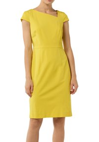 Gelbes, enges Kleid mit kurzärmeligen Puffärmelchen, schulterfreiem Ausschnitt und klarer Silhouette. Hergestellt aus glattem Stoff mit dezenten Nähten.