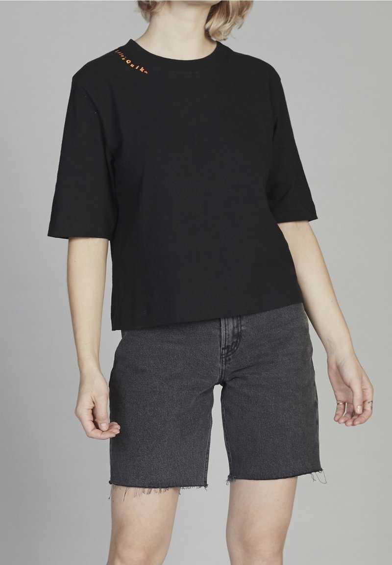 Camiseta de algodón negra de manga corta, con detalle de texto naranja en el hombro, combinada con pantalones cortos de mezclilla gris oscuro con dobladillo deshilachado.