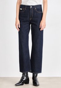 Mörkblå högmidjade vida jeans i denim, med kontrastsöm och framfickor. Bärs med svarta klackboots vid vristen.